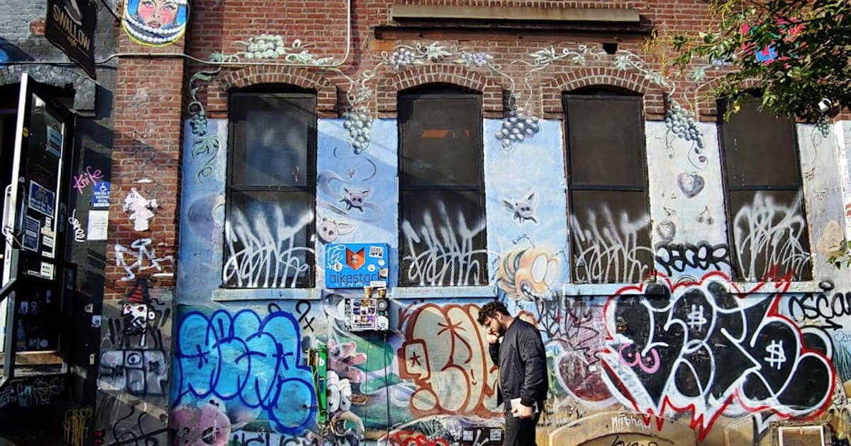Vibrant graffiti alley in Brooklyn with a person walking by, capturing urban street art culture.