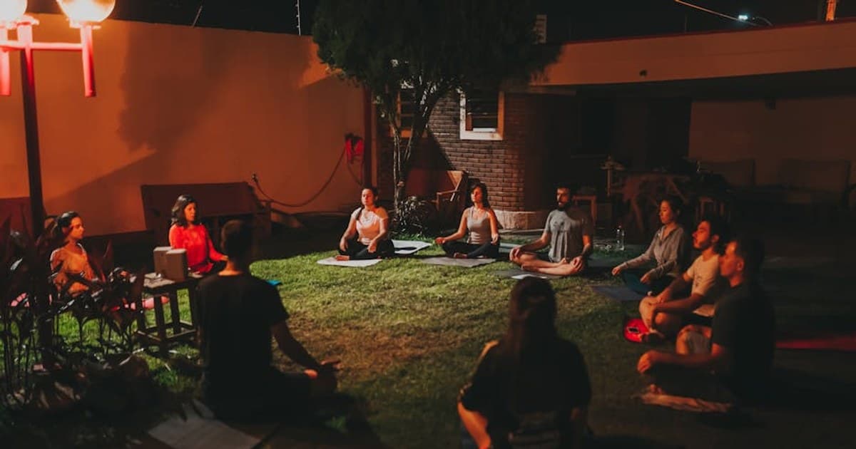A tranquil evening yoga class with diverse adults meditating outdoors on mats.