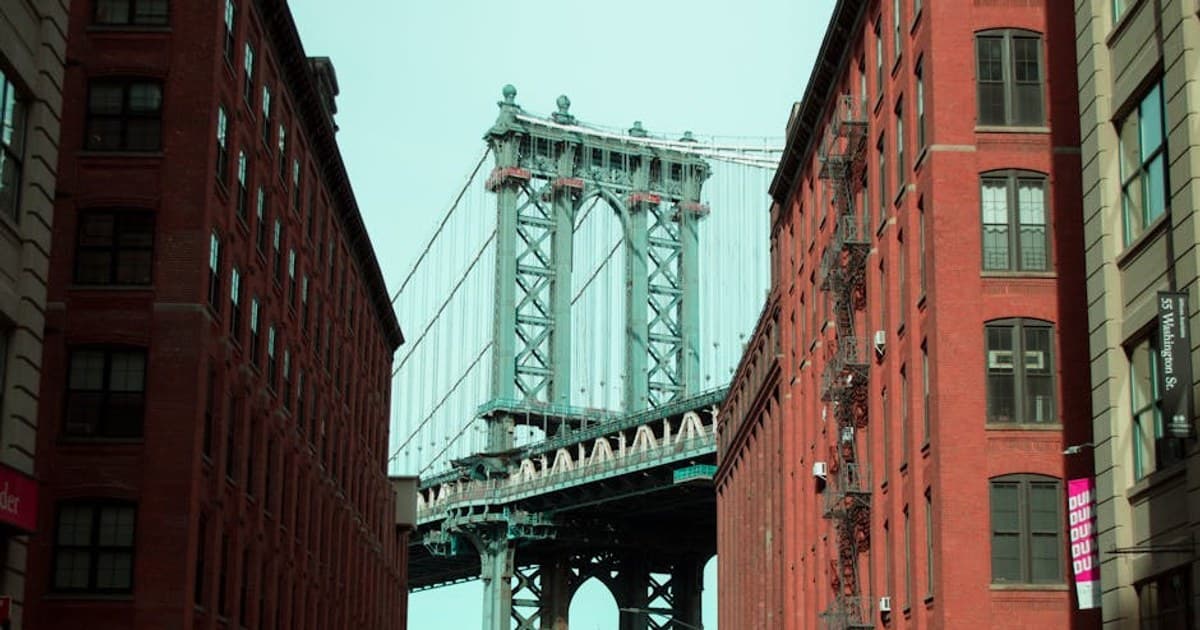An iconic view of the Manhattan Bridge framed by red brick buildings in Brooklyn, New York.