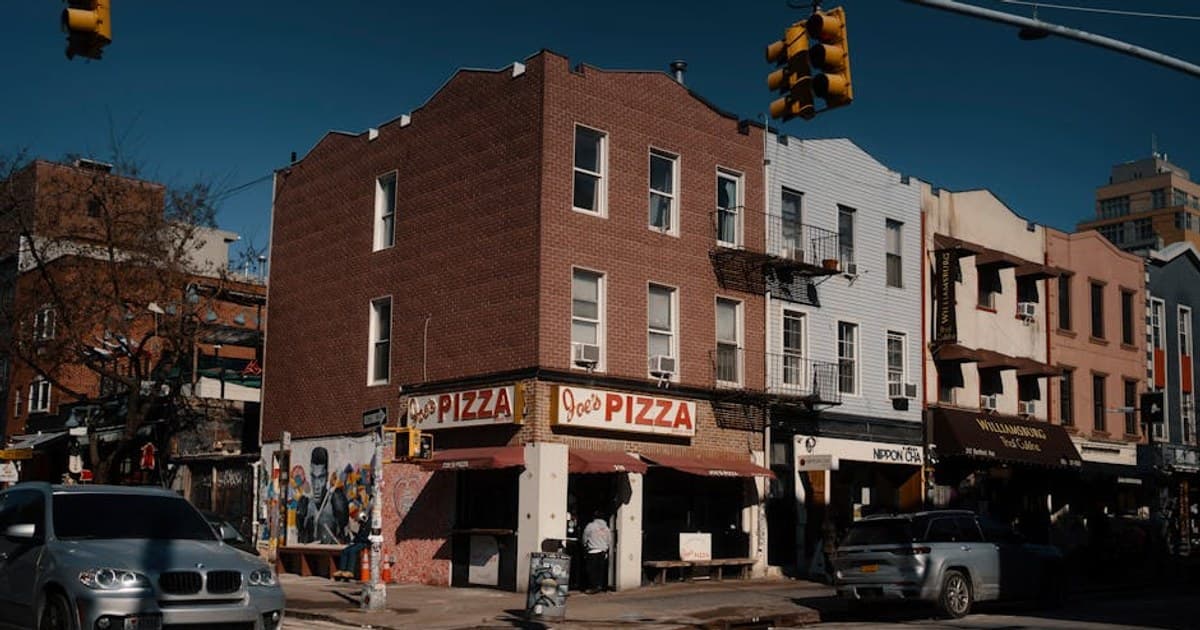 Street view of Joe's Pizza on a sunny day in Brooklyn, showcasing the lively urban atmosphere.