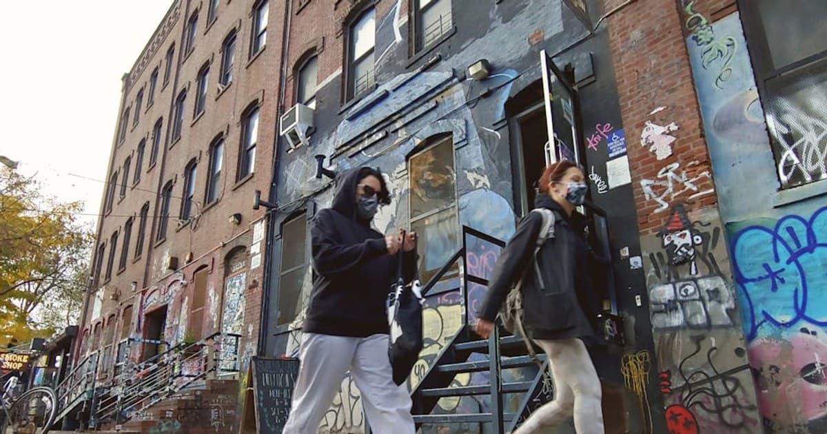 People walking past a graffiti-covered building in Brooklyn, New York.