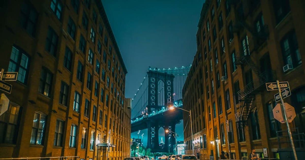 A captivating night view of the Brooklyn Bridge framed by urban buildings with ambient city lights.