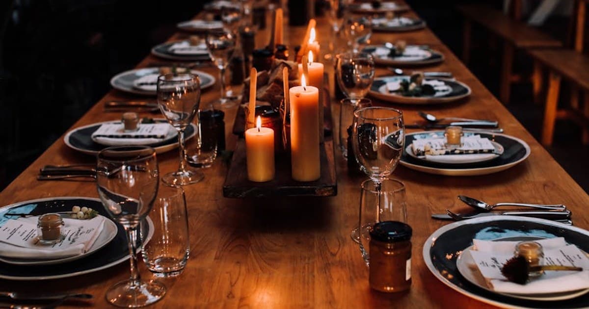 From above of long wooden banquet table with plates with decoration and name cards near glassware among burning candles in hall
