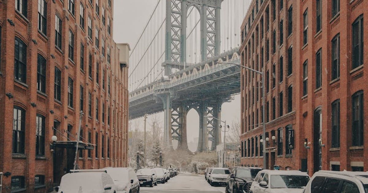 A classic view of the Manhattan Bridge framed by red brick buildings during a snowy winter day in New York City.