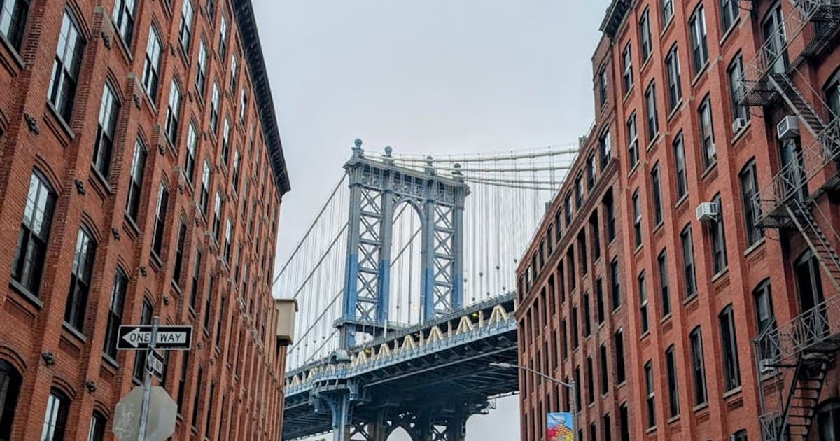 View of the Manhattan Bridge framed by red brick buildings in Brooklyn, New York.