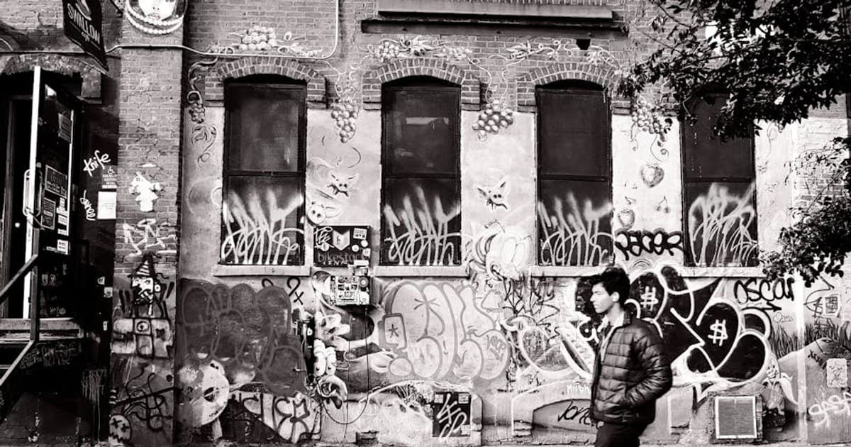 Black and white photo of a person walking by graffiti-covered building in Brooklyn, NYC.