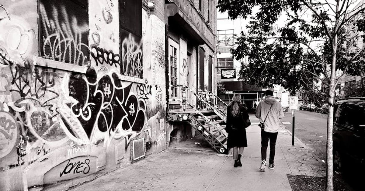 Black and white photo of a graffiti-filled alley with people walking in Brooklyn, New York.