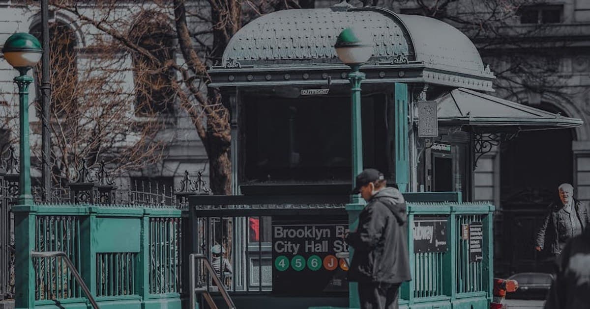 Full body of anonymous male in hat standing on street near green stall and stairway leading down in city district