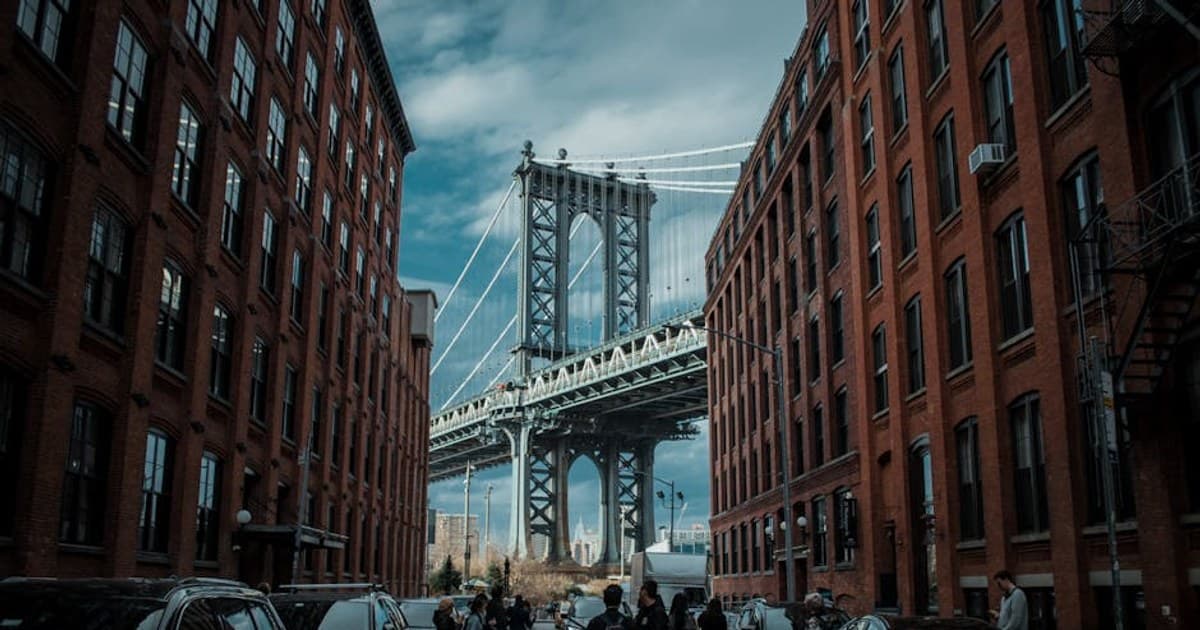 Street view under Manhattan Bridge with brick buildings and pedestrians in Dumbo, NYC.