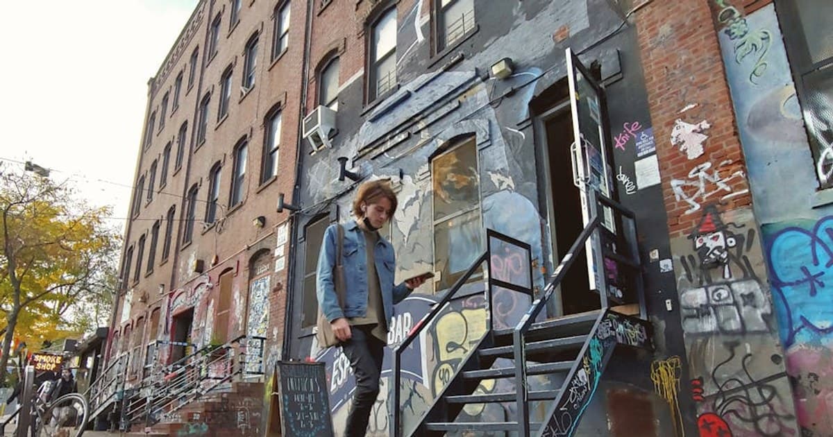 A person walking past graffiti-covered buildings on a vibrant street in Brooklyn.
