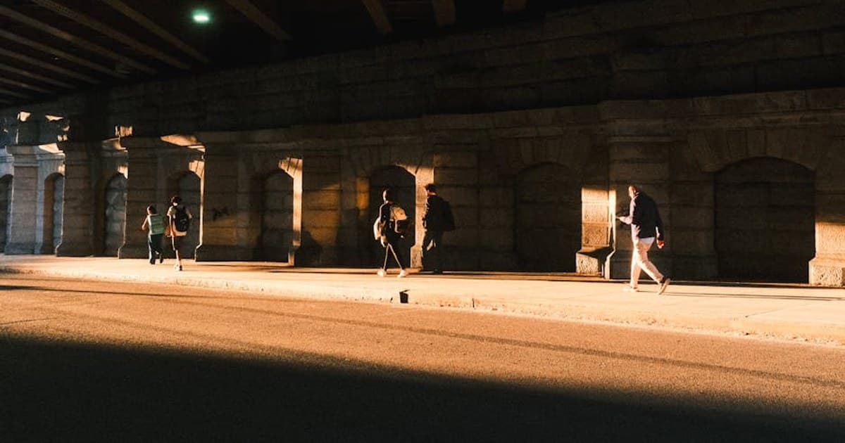 People walking under the Brooklyn Bridge in warm sunset light, capturing New York's urban atmosphere.