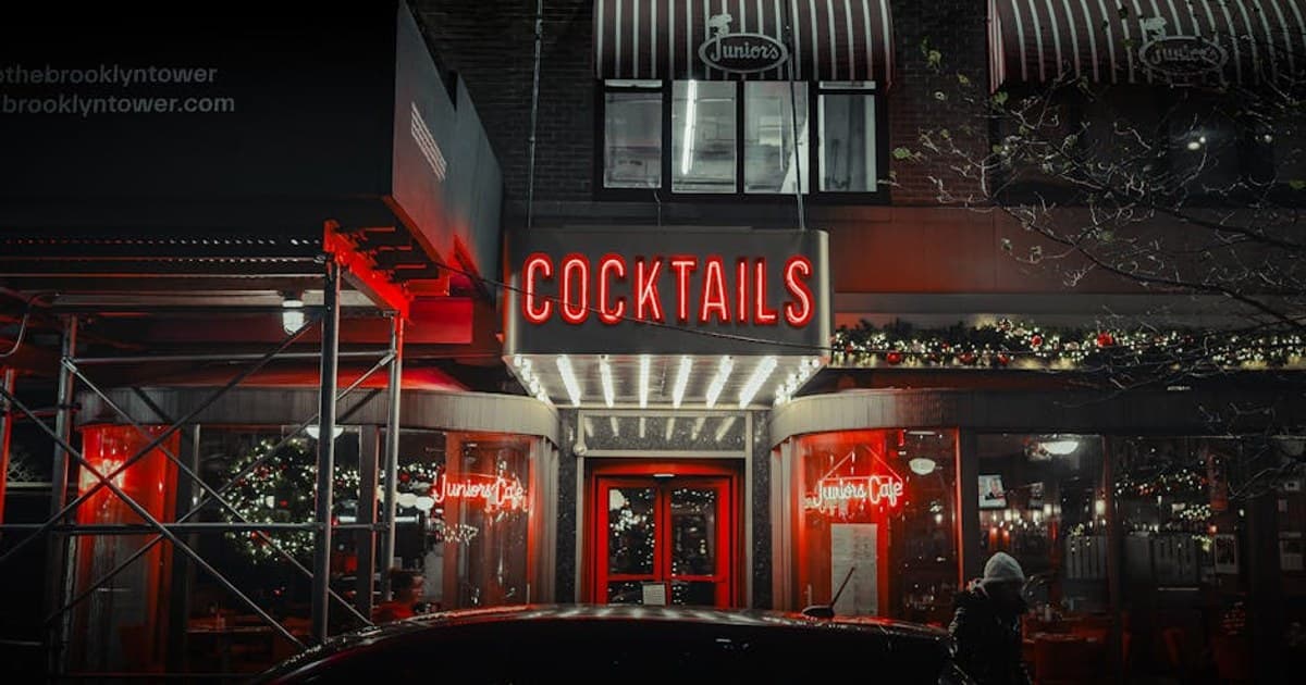 A neon-lit entrance of Juniors Cafe in NYC showcasing a vibrant nightlife scene with festive decorations.
