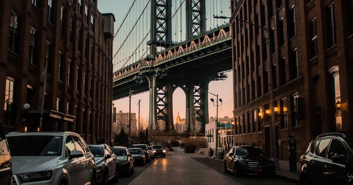 Urban scene with Manhattan Bridge framed by buildings and sunset glow.
