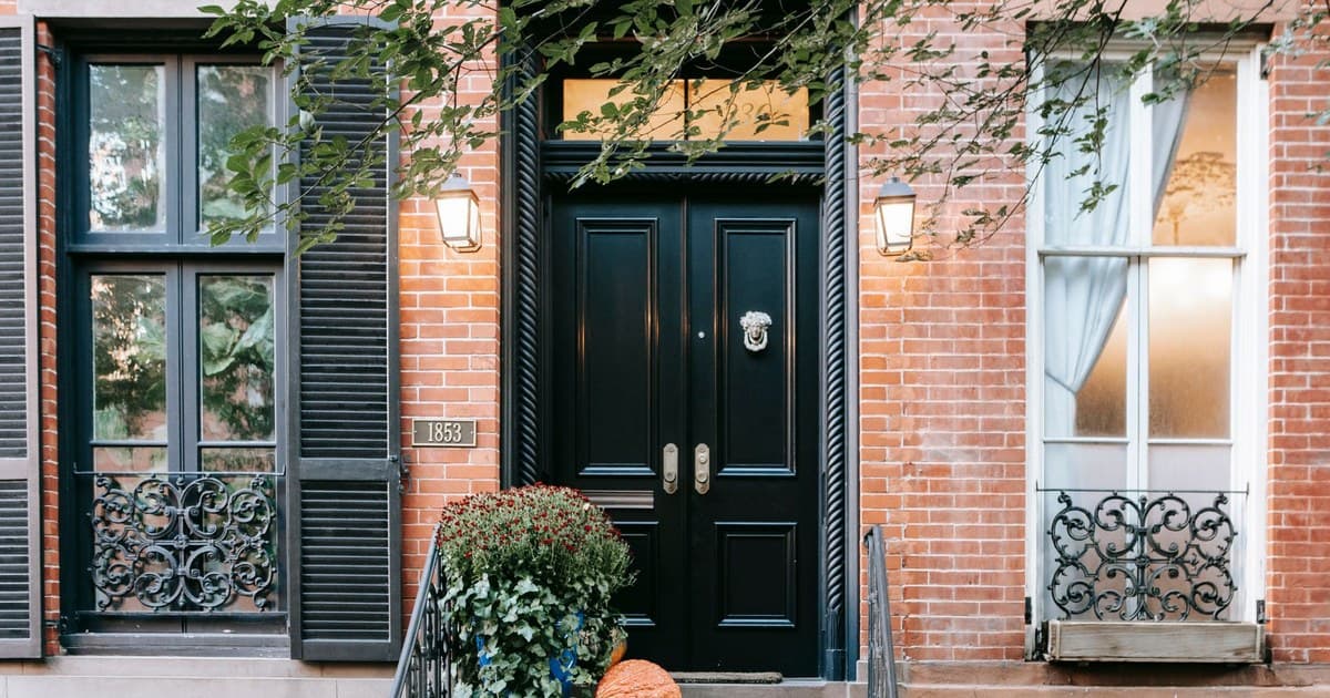 Entrance of residential building with pumpkins on stone stairway near black door and windows on brick wall located in street