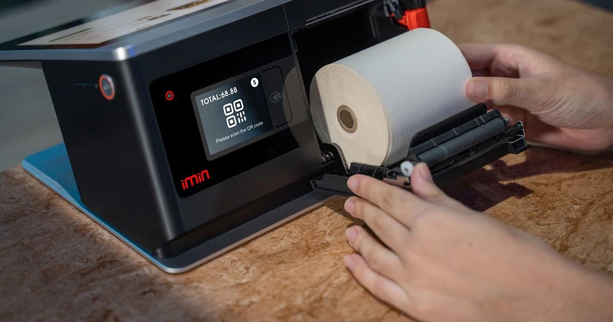 Hands setting up a thermal roll in a point-of-sale touchscreen device.